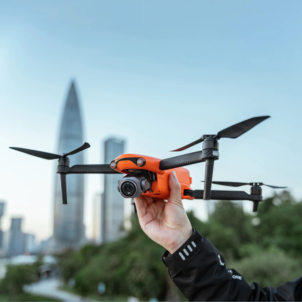 Drone orange tenu devant la ligne d'horizon de la ville. Main tenant le drone. Fond de ciel clair.