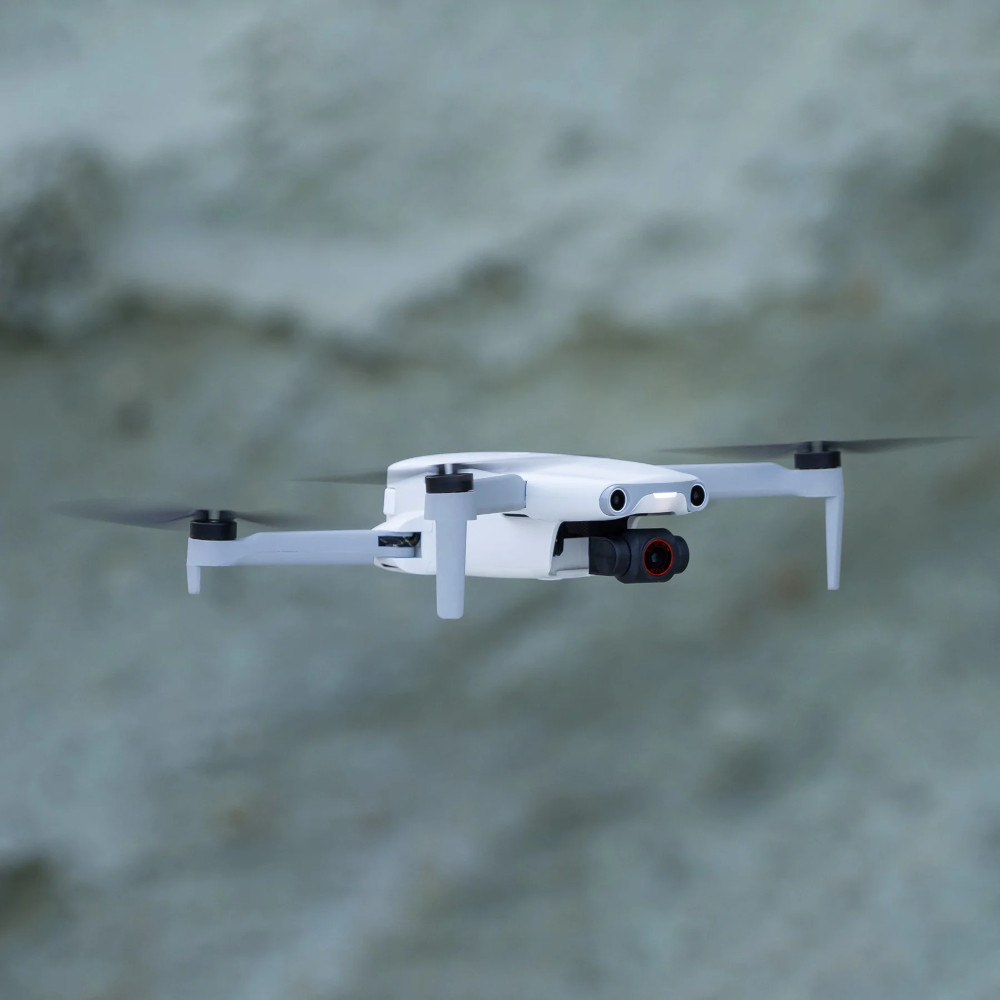 Drone blanc en vol. Hélices noires et une caméra rouge.