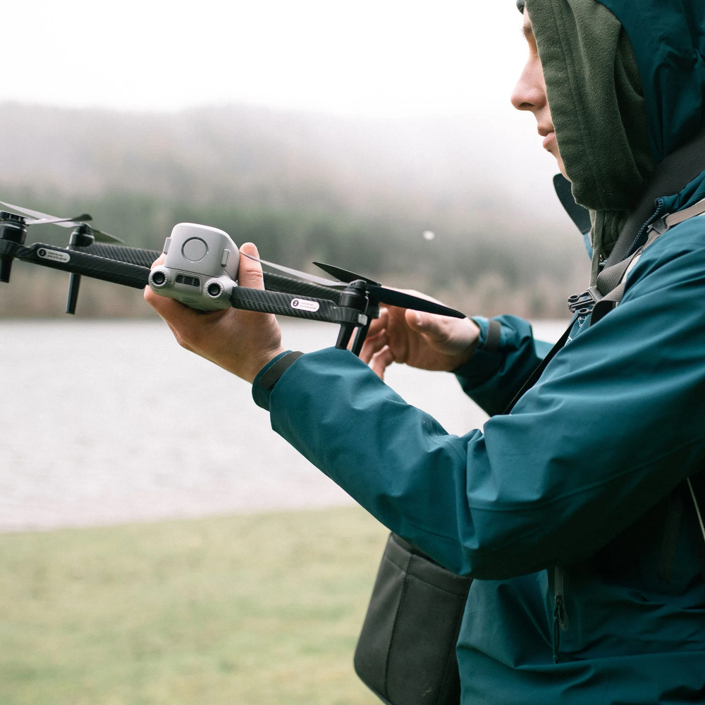 Een persoon die een grijze drone vasthoudt. De persoon draagt een blauwe jas.