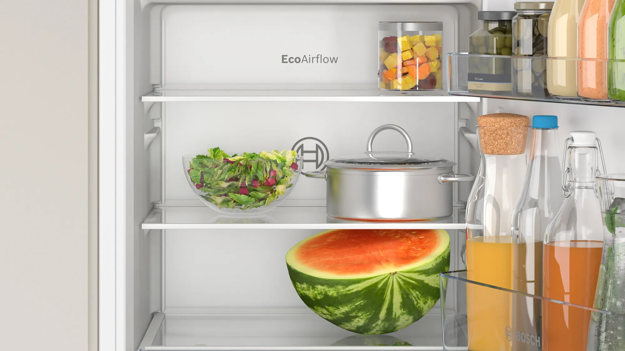 Binnen in een koelkast: salade, watermeloen, potten en een pan zijn zichtbaar op de planken.