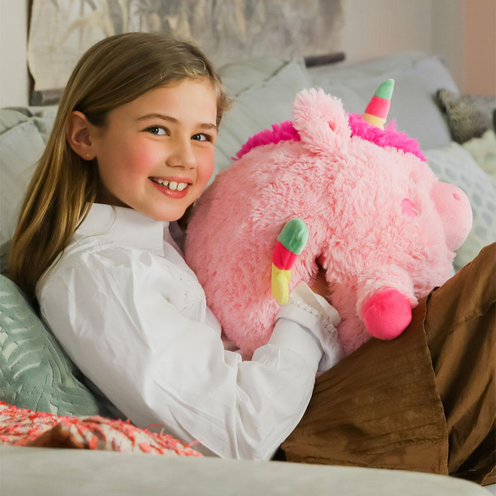 Ein Mädchen mit einem rosa Einhorn-Plüschtier sitzt auf einem Sofa. Sie lächelt.