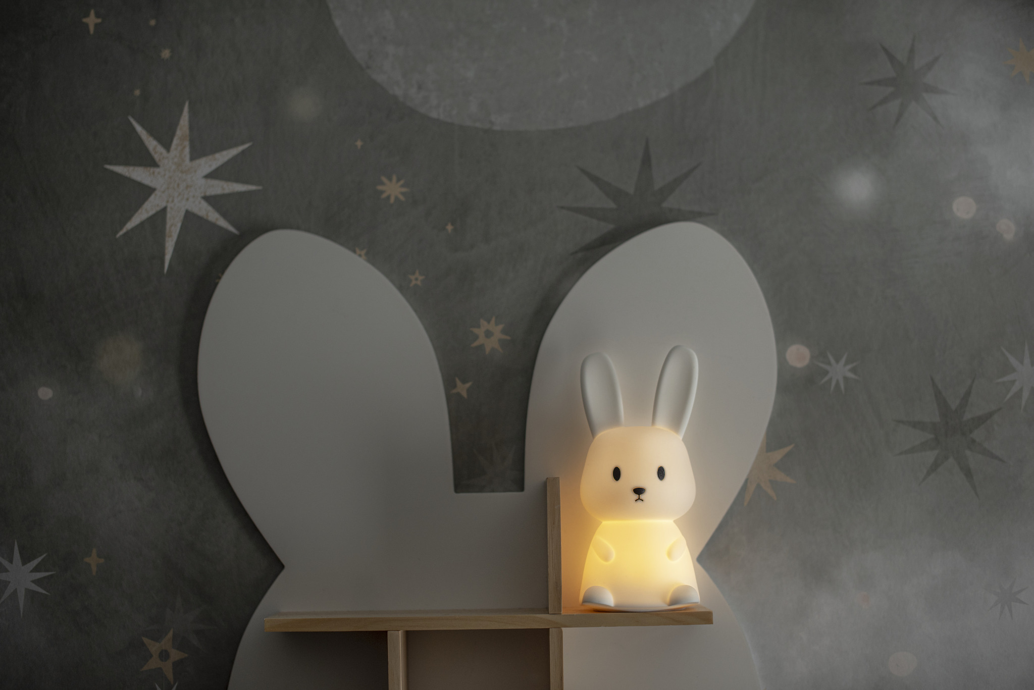 Luce notturna a forma di coniglietto bianco su una mensola. Parete grigia con motivi a stella.