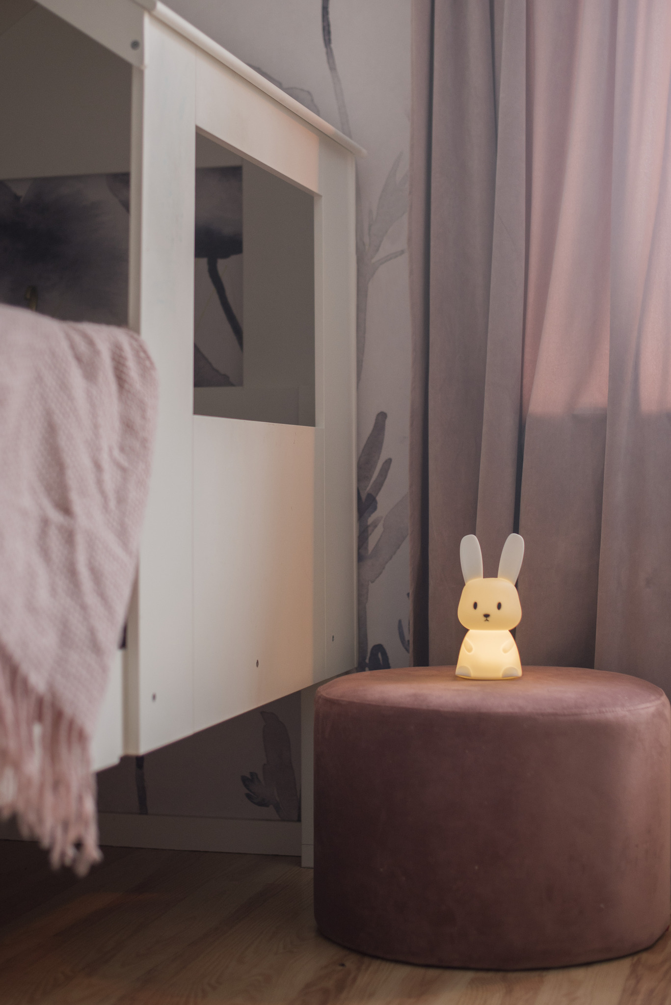 Lampada a forma di coniglio su un pouf marrone vicino a un letto.