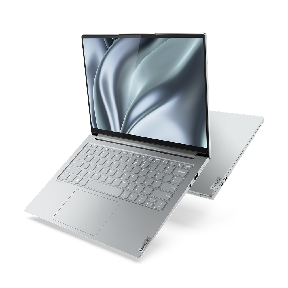 Portátil Lenovo plateado con teclado gris claro, abierto sobre una superficie negra, segundo portátil en el fondo.