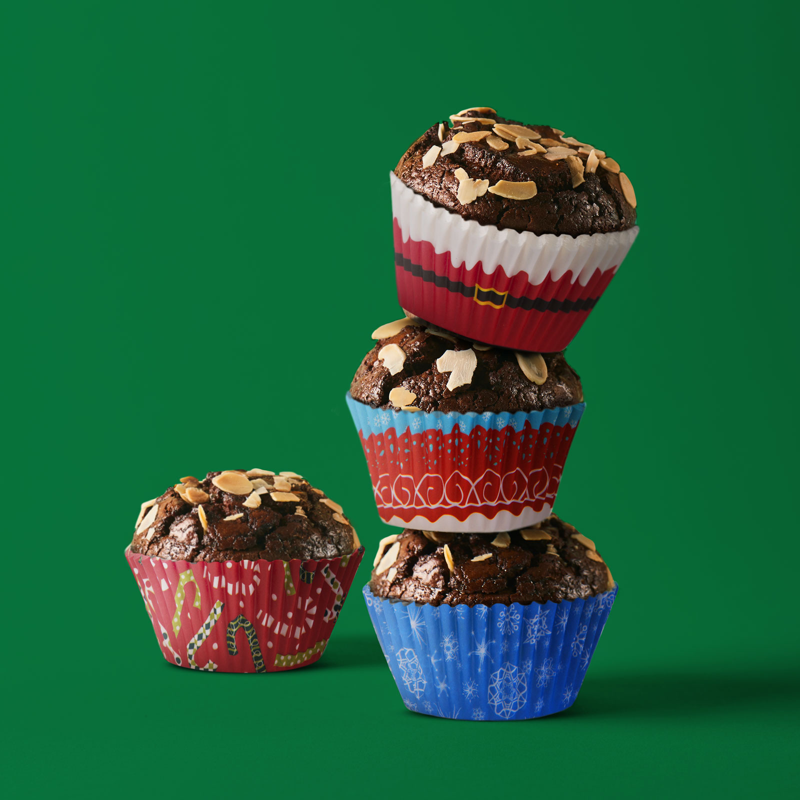 Négy muffin egymásra rakva, mandulapehellyel. Mindegyik színes papírban. Zöld háttér.