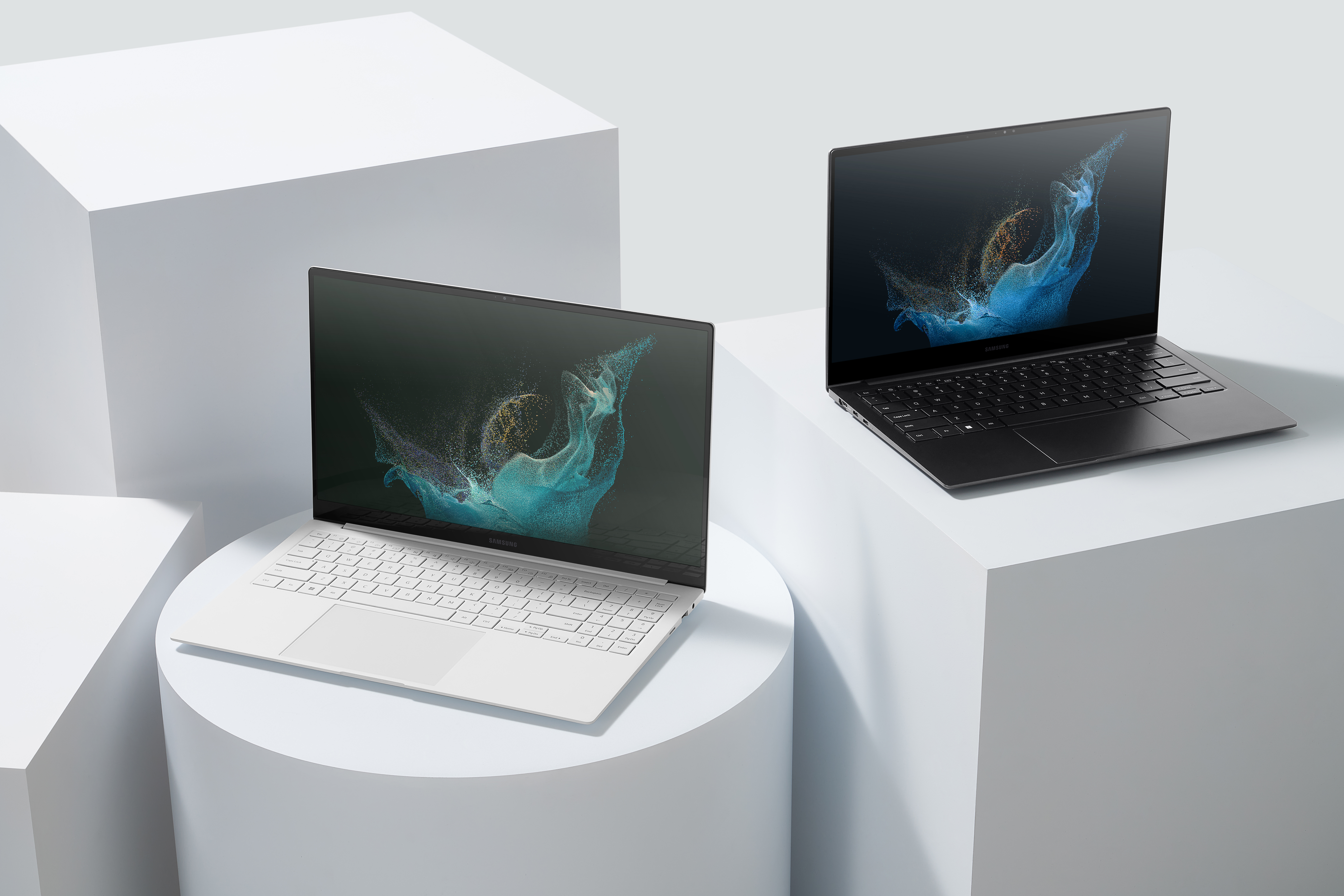 Dos portátiles modernos sobre plataforma blanca, uno abierto, con arte en pantalla.