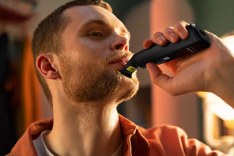 Man scheert zijn baard met een zwart-gele trimmer. Close-up, wazige achtergrond.