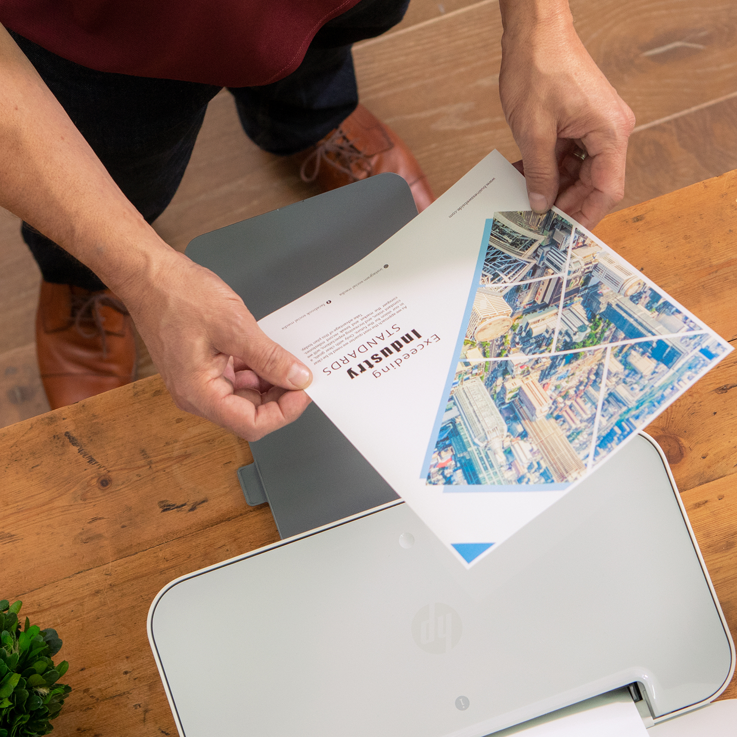 Handen die een document boven een printer op een houten tafel houden. Het document heeft een stadsafbeelding.