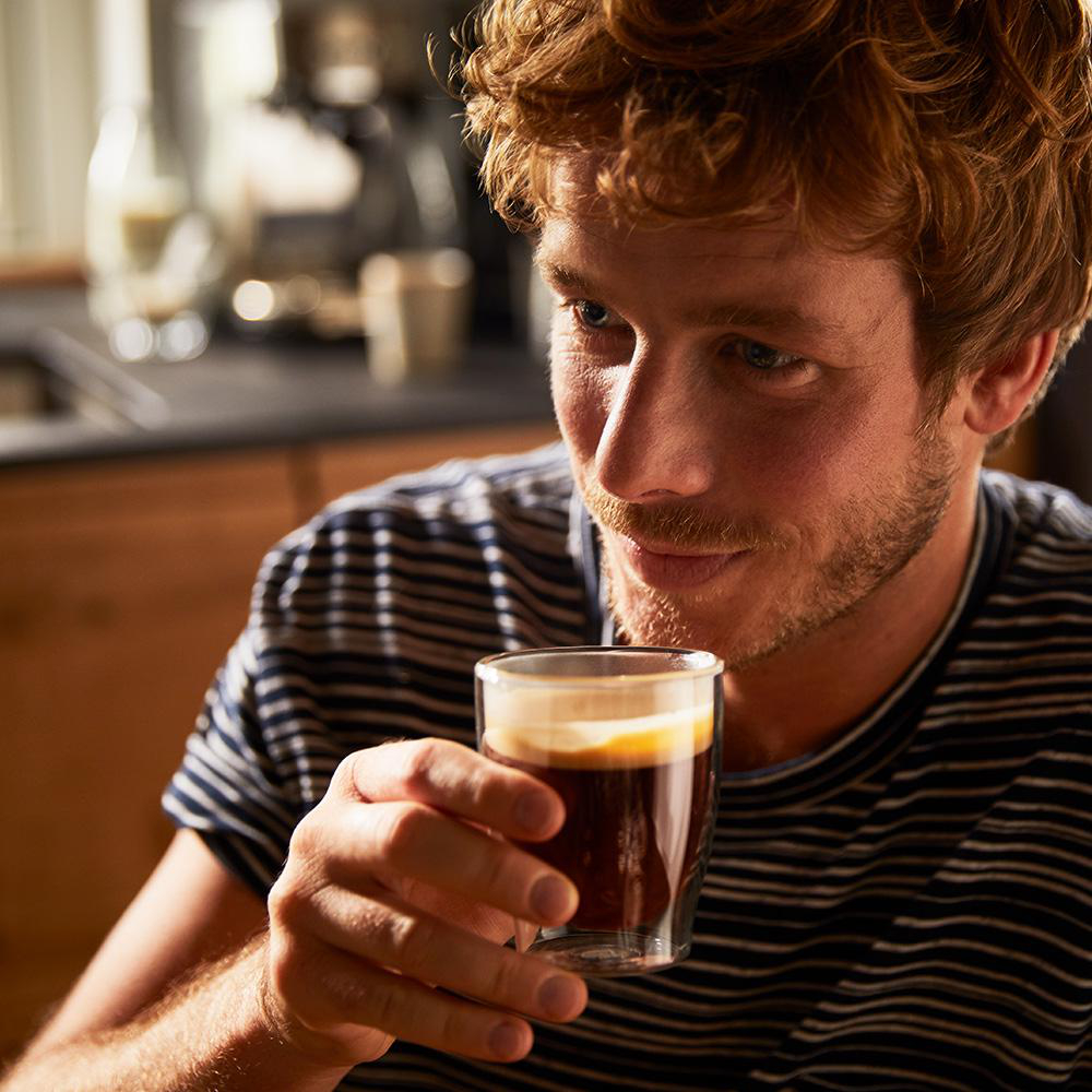 Ein Mann hält ein Glas Kaffee und betrachtet es mit nachdenklichem Ausdruck.