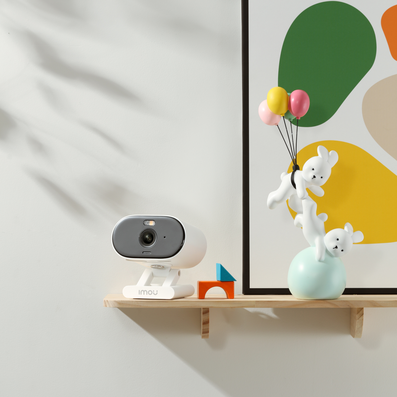 Une caméra domestique intelligente blanche sur une étagère avec des décorations colorées.