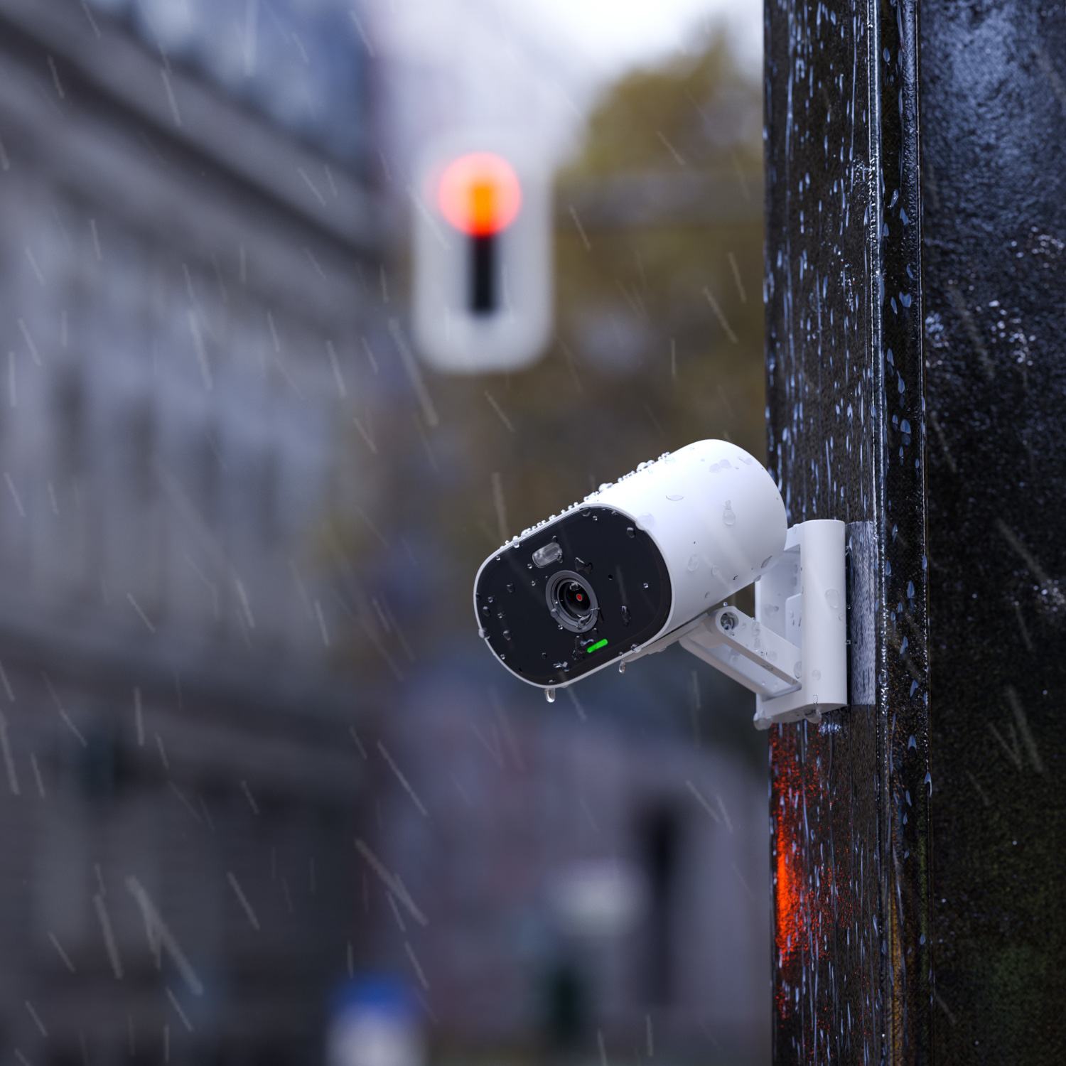 Une caméra de sécurité blanche montée sur un poteau noir sous la pluie, avec un feu rouge.