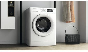 Witte Whirlpool wasmachine. Wasmand en kleding hangen aan de zijkant.