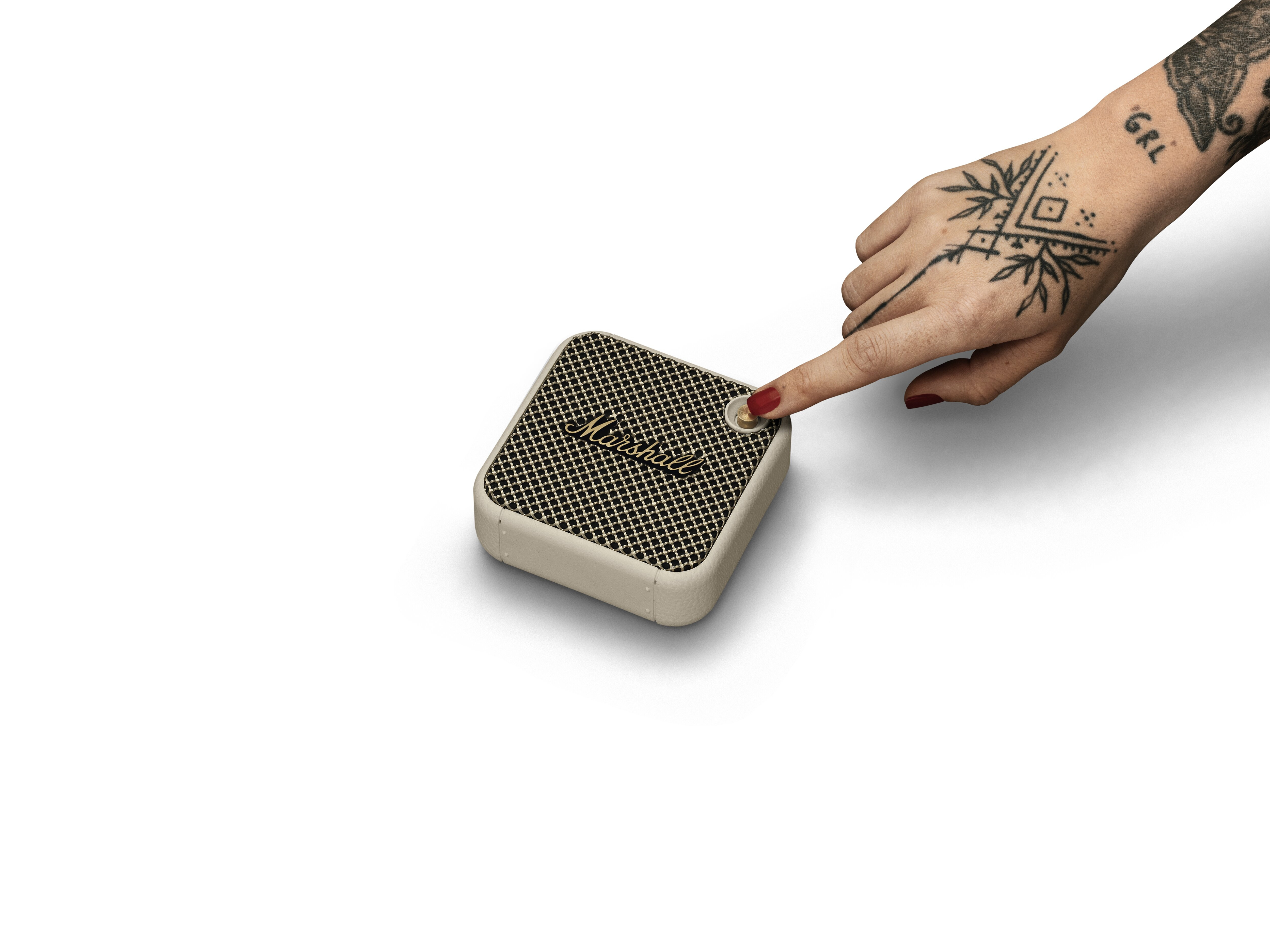 Eine Hand mit Tattoos drückt auf einen Knopf eines kleinen Lautsprechers mit dem Wort 'Marshall'.