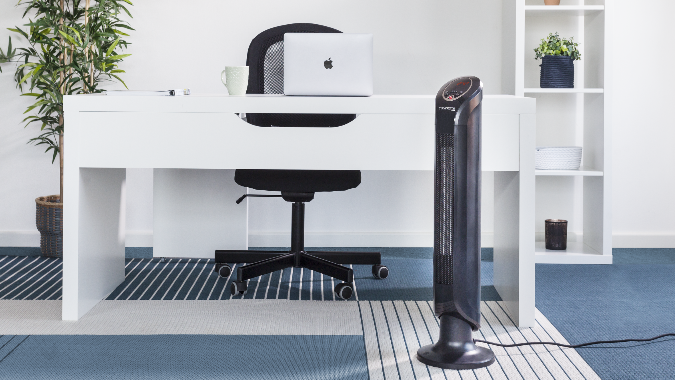 Un escritorio blanco con una laptop y una silla, y un ventilador de torre negro en un entorno de oficina en casa.