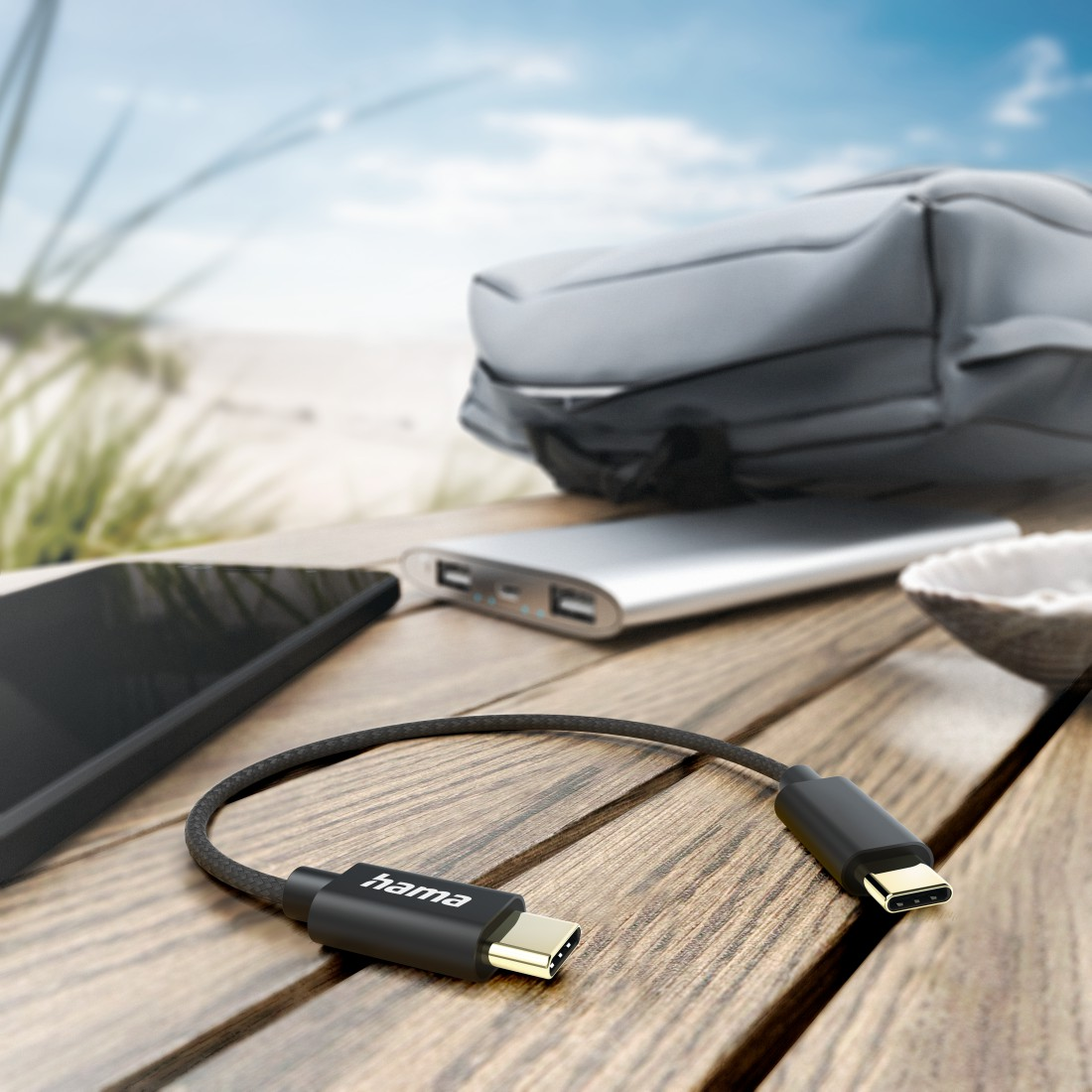 Schwarzes USB-C-Kabel verbunden mit Telefon, Powerbank und anderen Gegenständen, auf Holzoberfläche.