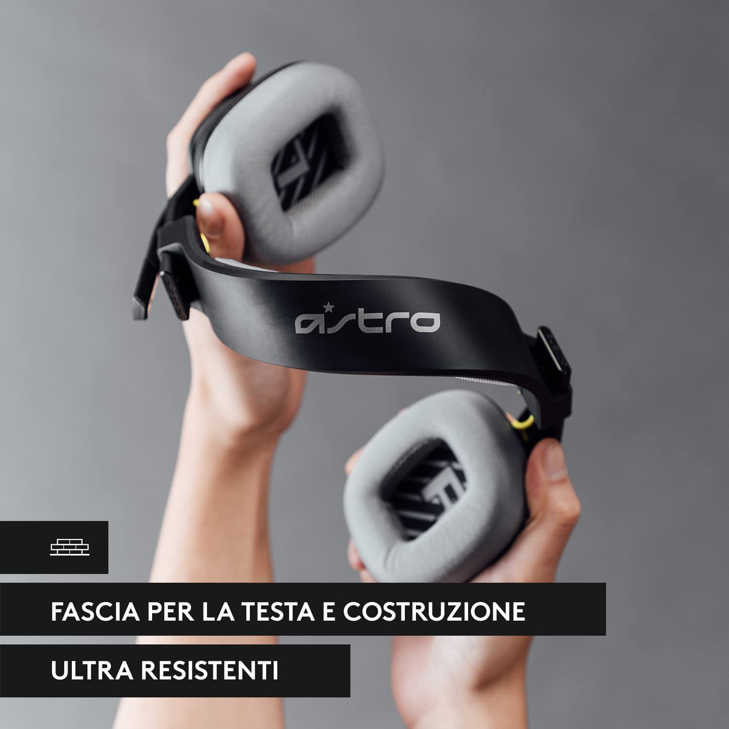 Cuffie in mano. Fascia nera con logo Astro, padiglioni grigi e dettagli gialli.