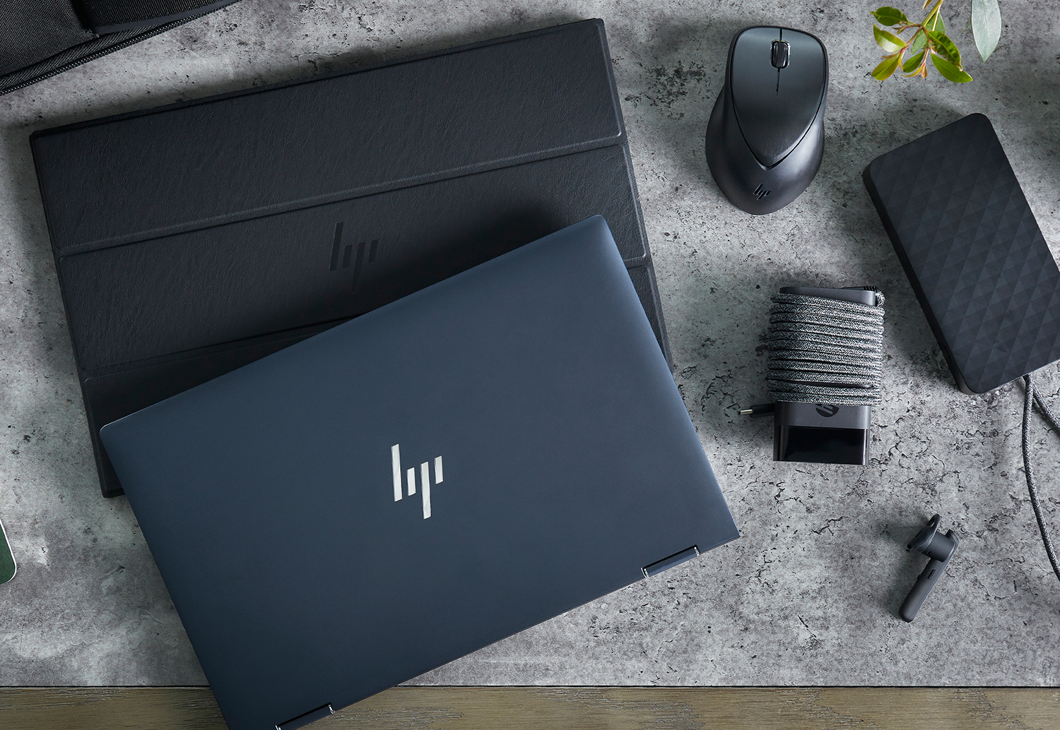 Laptop, hoes, muis en externe harde schijf op een grijs oppervlak. Kleine plant op de achtergrond.