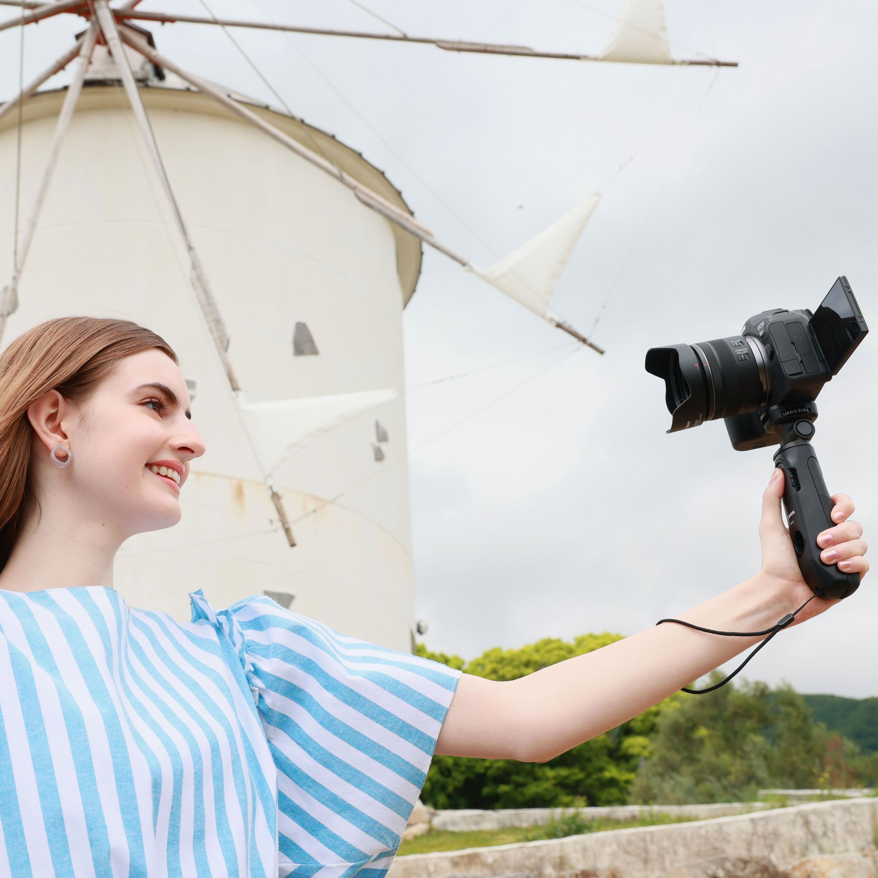 Una donna con un top a righe blu e bianche si riprende con una telecamera su impugnatura, con un mulino a vento.