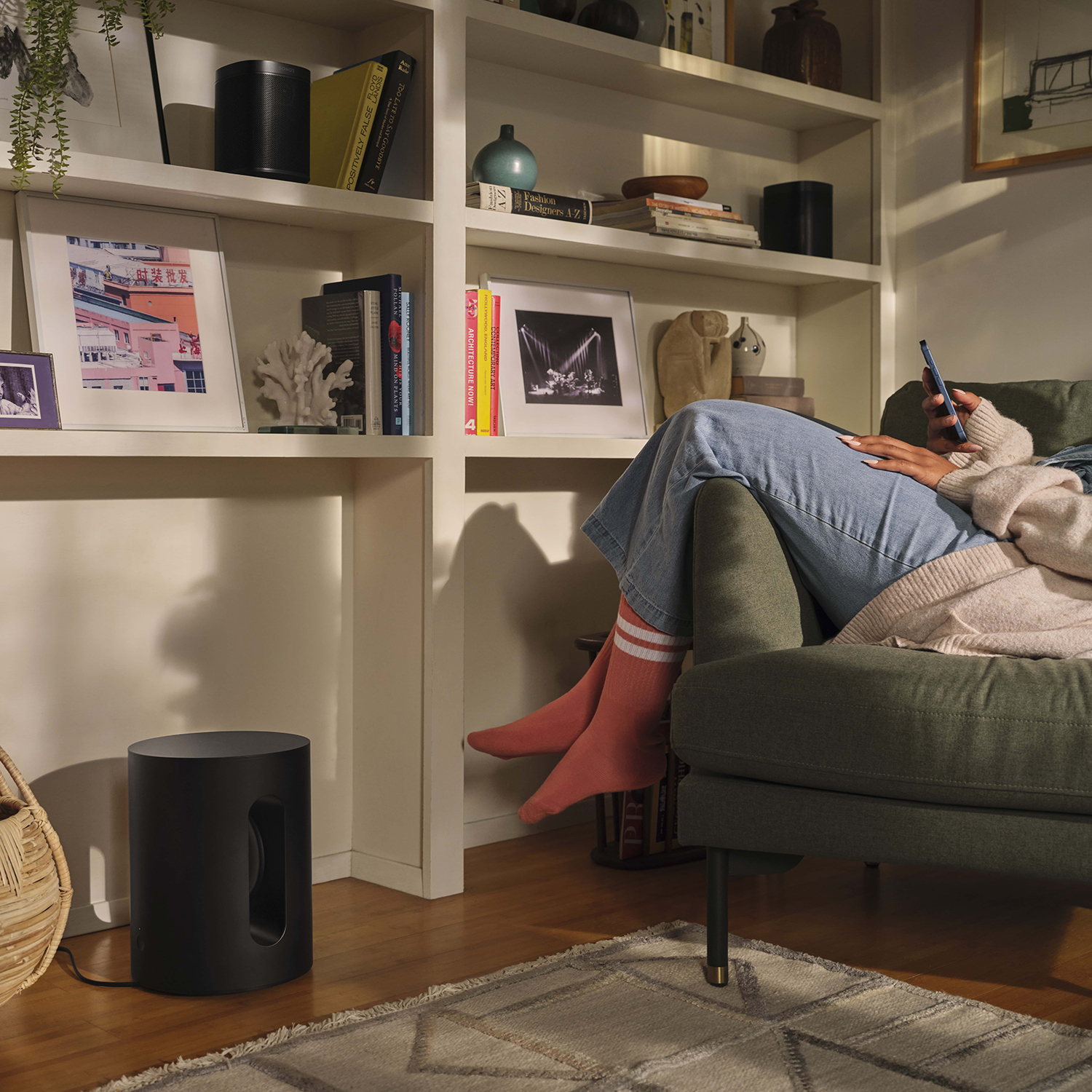 Una persona seduta su un divano verde con un telefono, con un subwoofer nero.