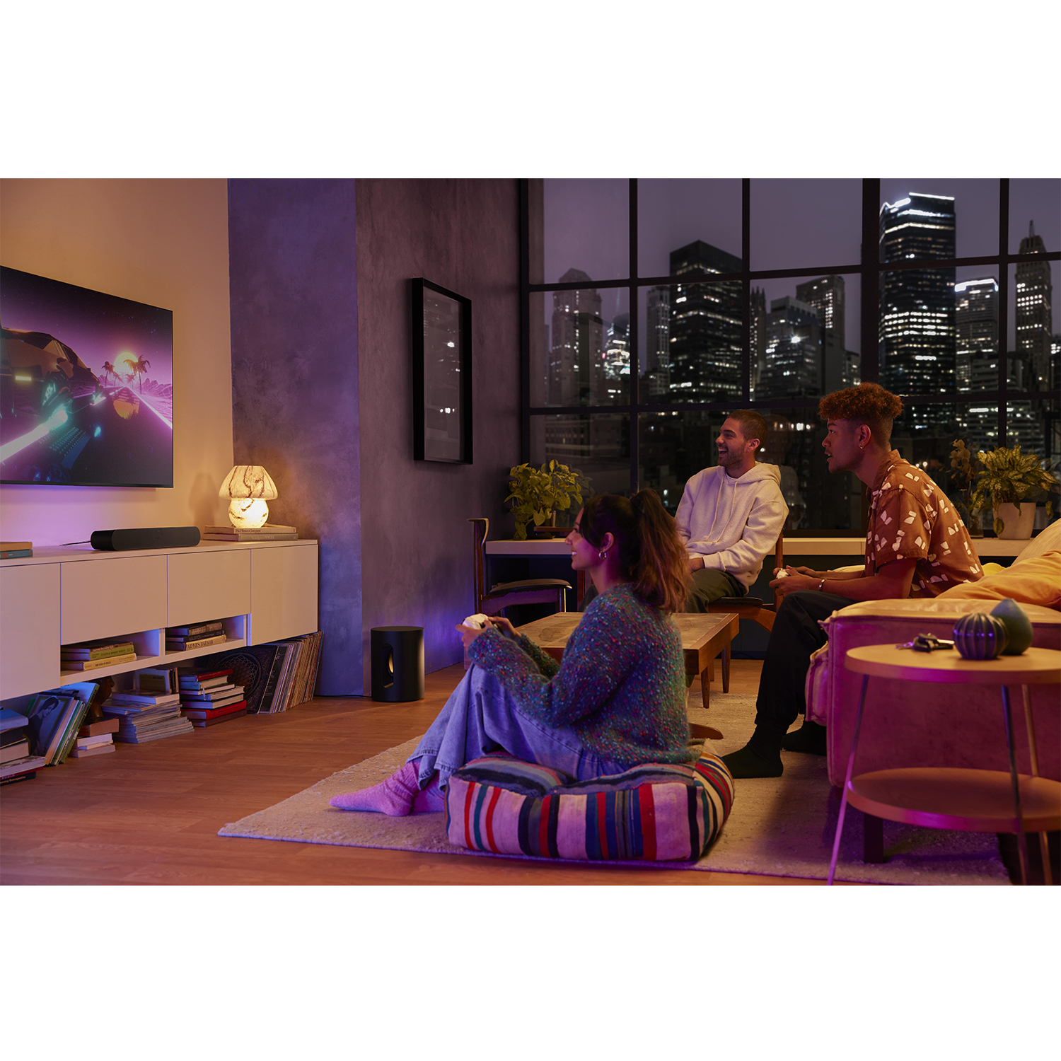 Tre persone sedute, che giocano ai videogiochi, guardano la TV, di notte.