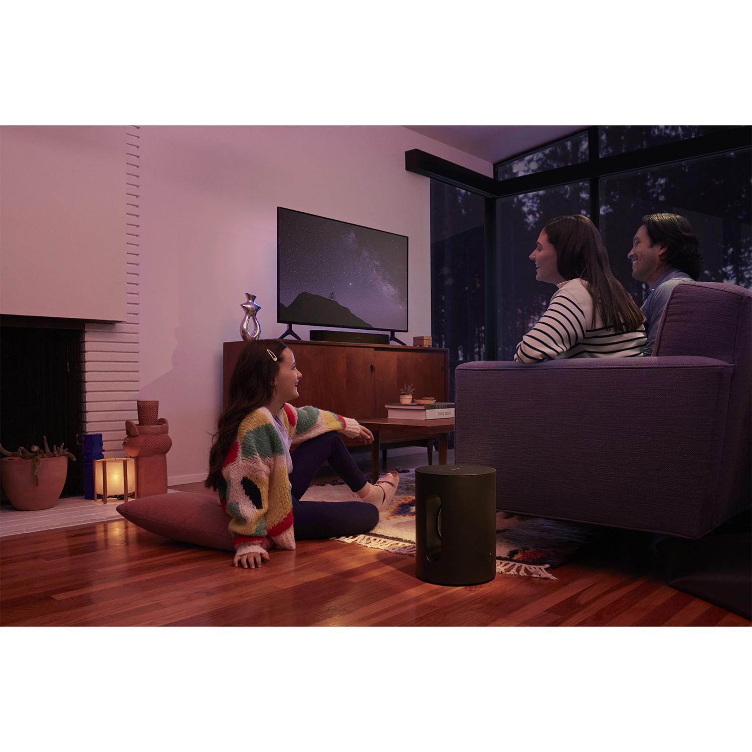 Una famiglia in soggiorno, che guarda la TV, con una soundbar e un altoparlante.