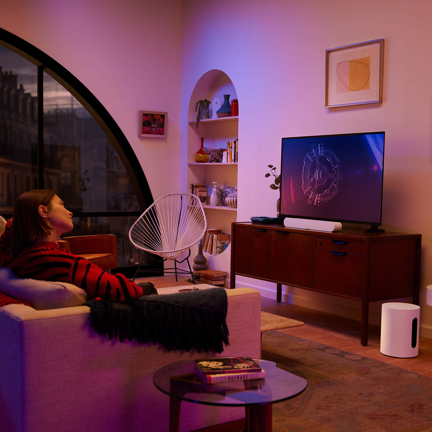 Una donna su un divano che guarda la TV con una soundbar e un subwoofer in una stanza con opere d'arte.