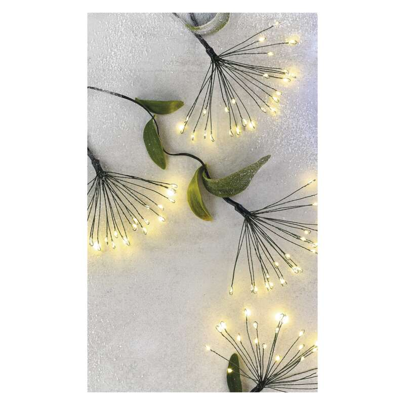 Közelkép a díszvilágításról az ágakon. Ágak apró fényekkel és zöld levelekkel.