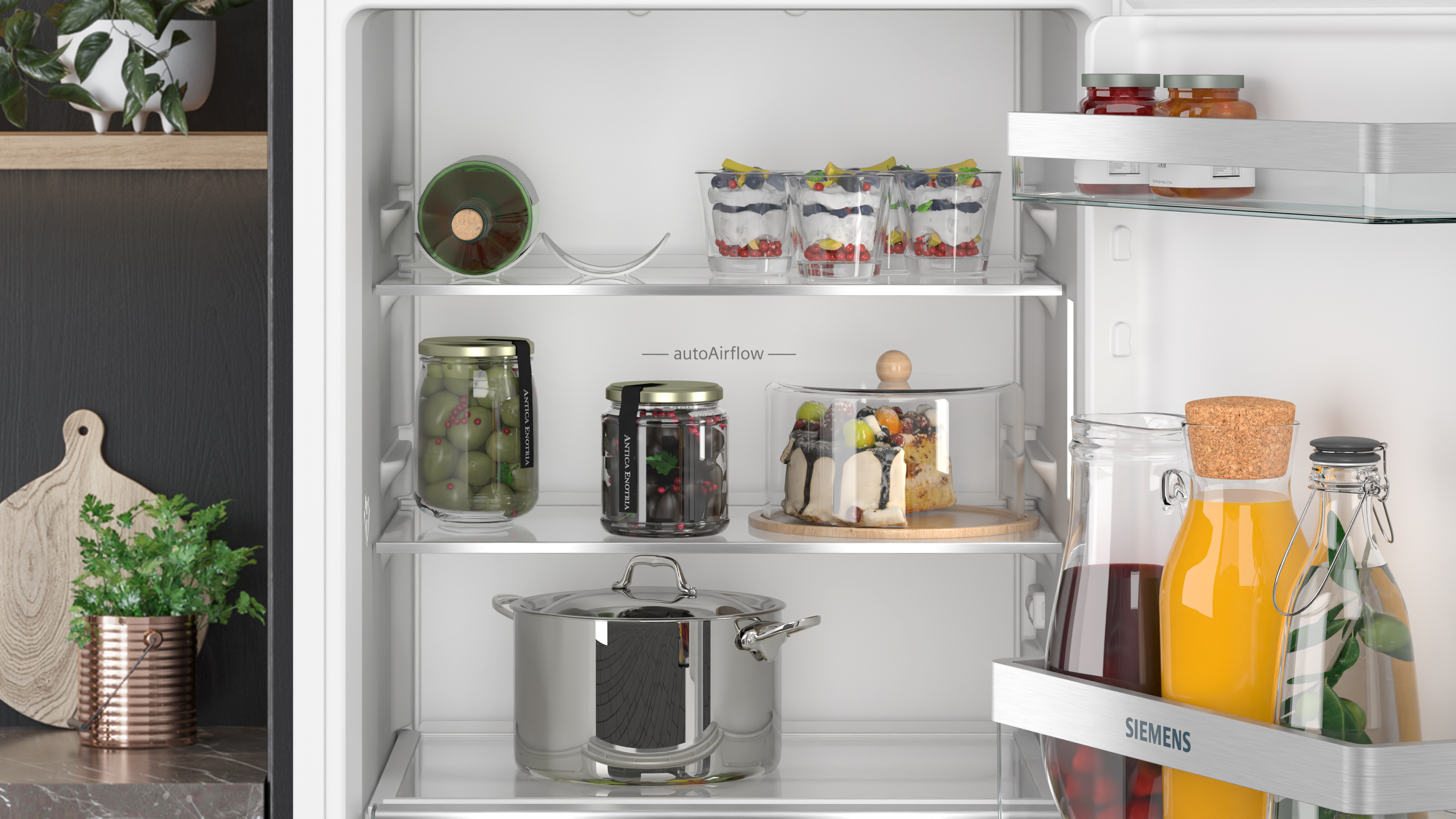 Fridge interior with food items on shelves. Jars, fruits, desserts, and a pot. White interior.