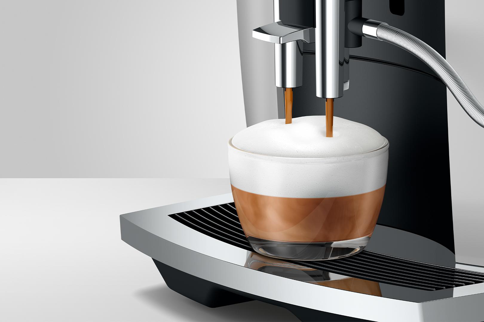 Eine Kaffeemaschine, die Kaffee in eine gläserne Tasse mit Milchschaum ausgibt.