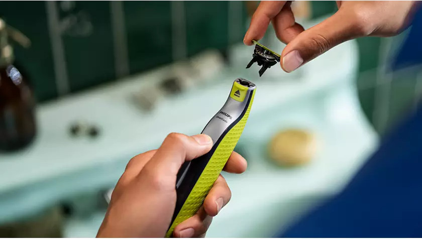 Les mains d'une personne changent une tête de rasoir. Le rasoir est noir et vert citron.