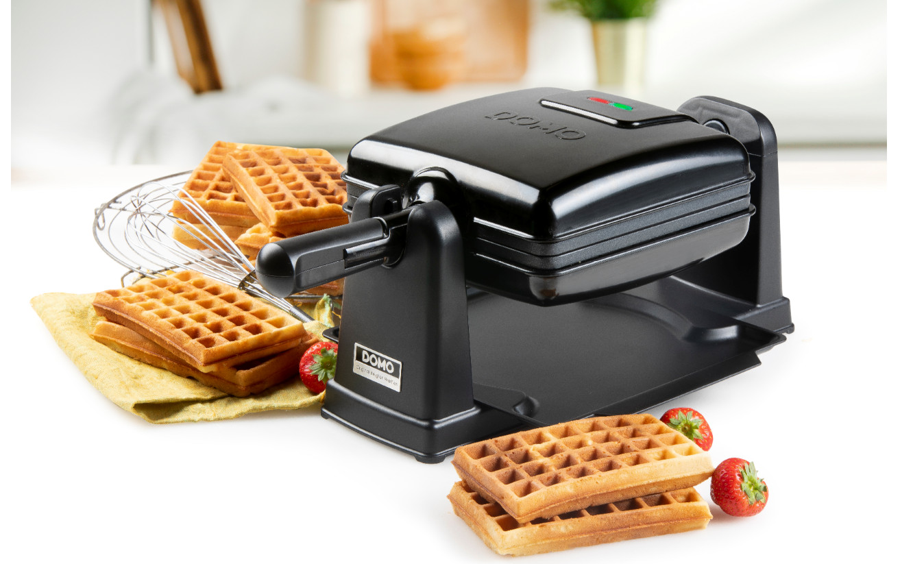 Waffle maker with waffles and strawberries. Metal whisk. Waffles stacked and next to the maker.