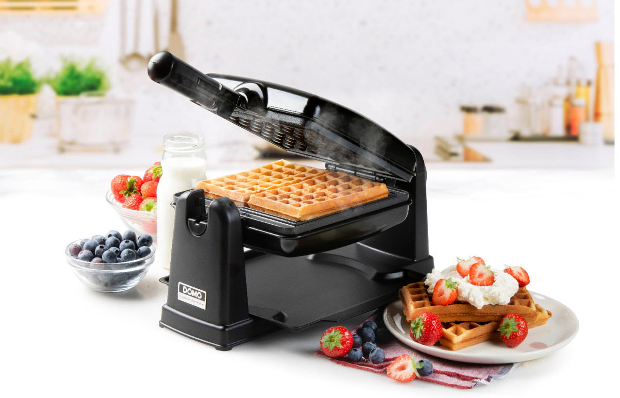 Black waffle maker with cooked waffles and toppings.