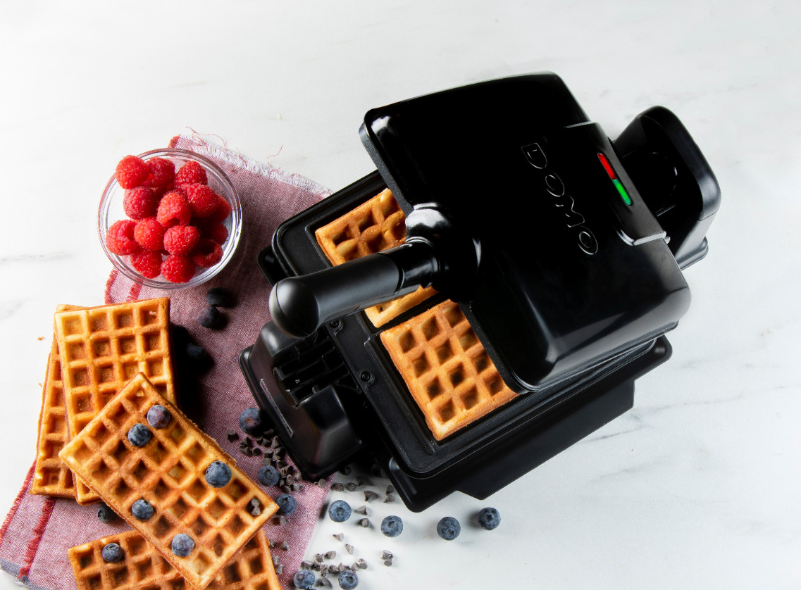 Waffles in a waffle maker. Raspberries and blueberries are nearby.