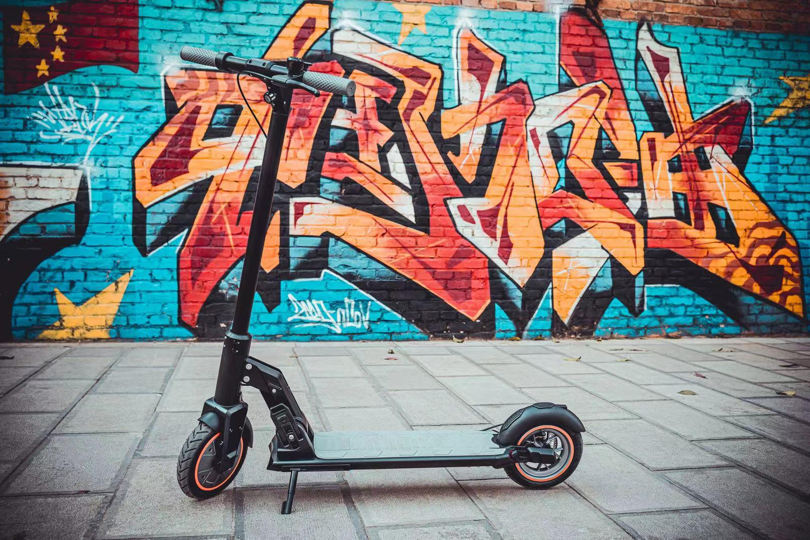Graffiti ile kaplı bir tuğla duvarın önünde park etmiş siyah bir scooter.