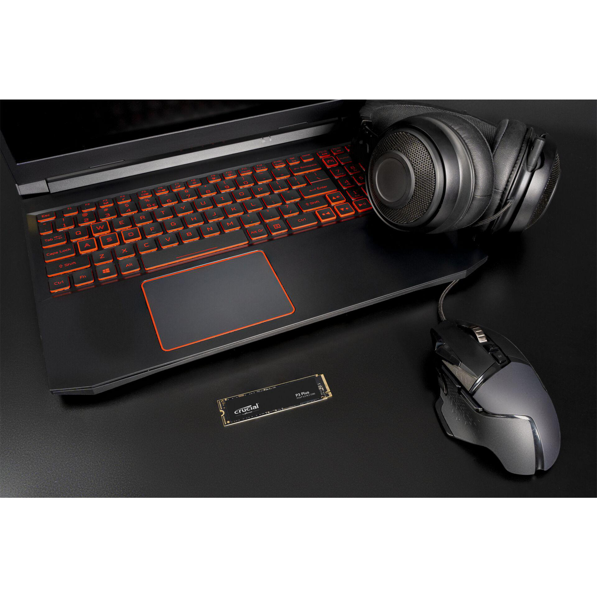 Laptop, Kopfhörer, Maus und SSD auf schwarzer Oberfläche. Die Laptop-Tastatur hat eine orangefarbene Hintergrundbeleuchtung.