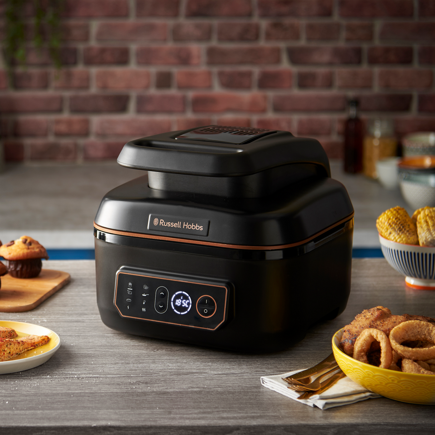 Zwarte Russell Hobbs airfryer met een digitaal display, omringd door eten op een houten tafel.