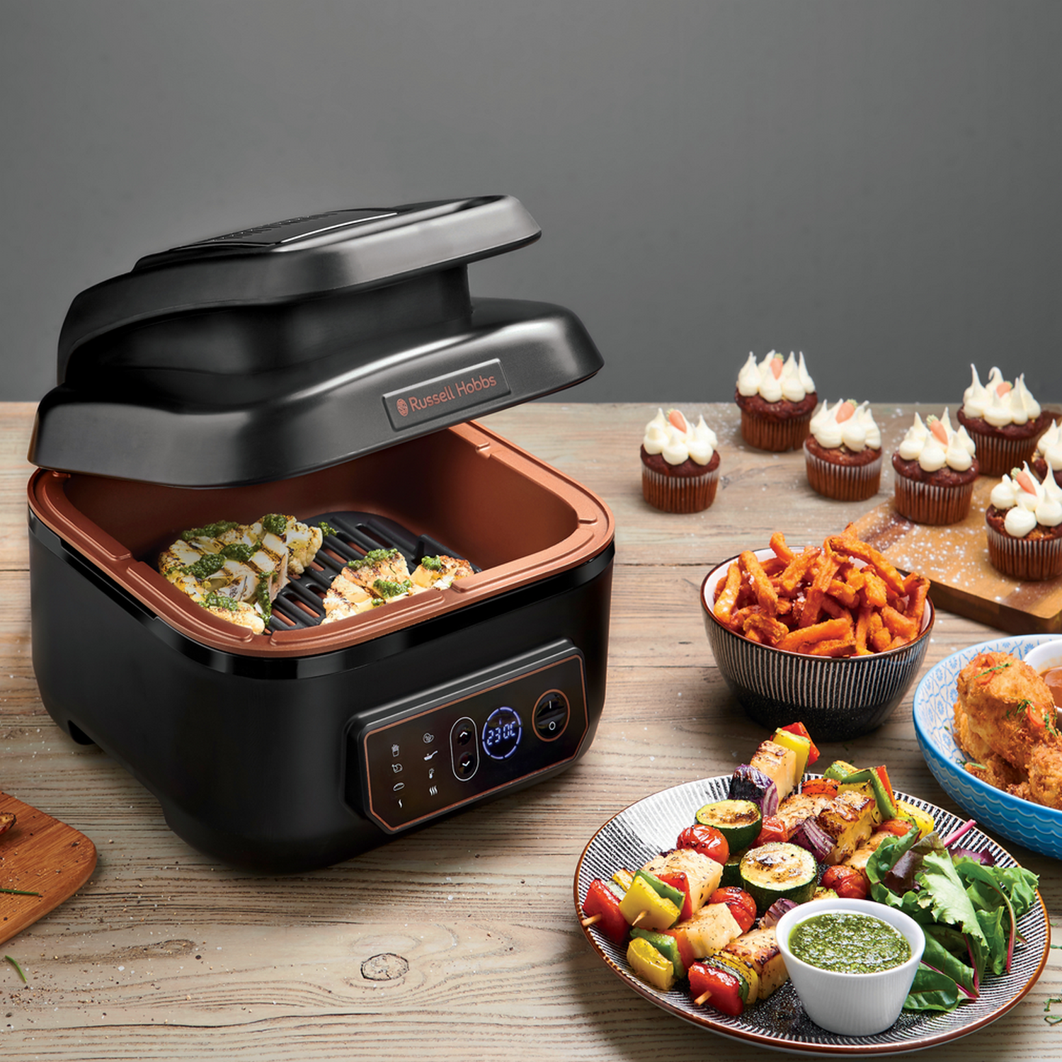 Russell Hobbs grill met gekookt eten en cupcakes, met divers eten op tafel.