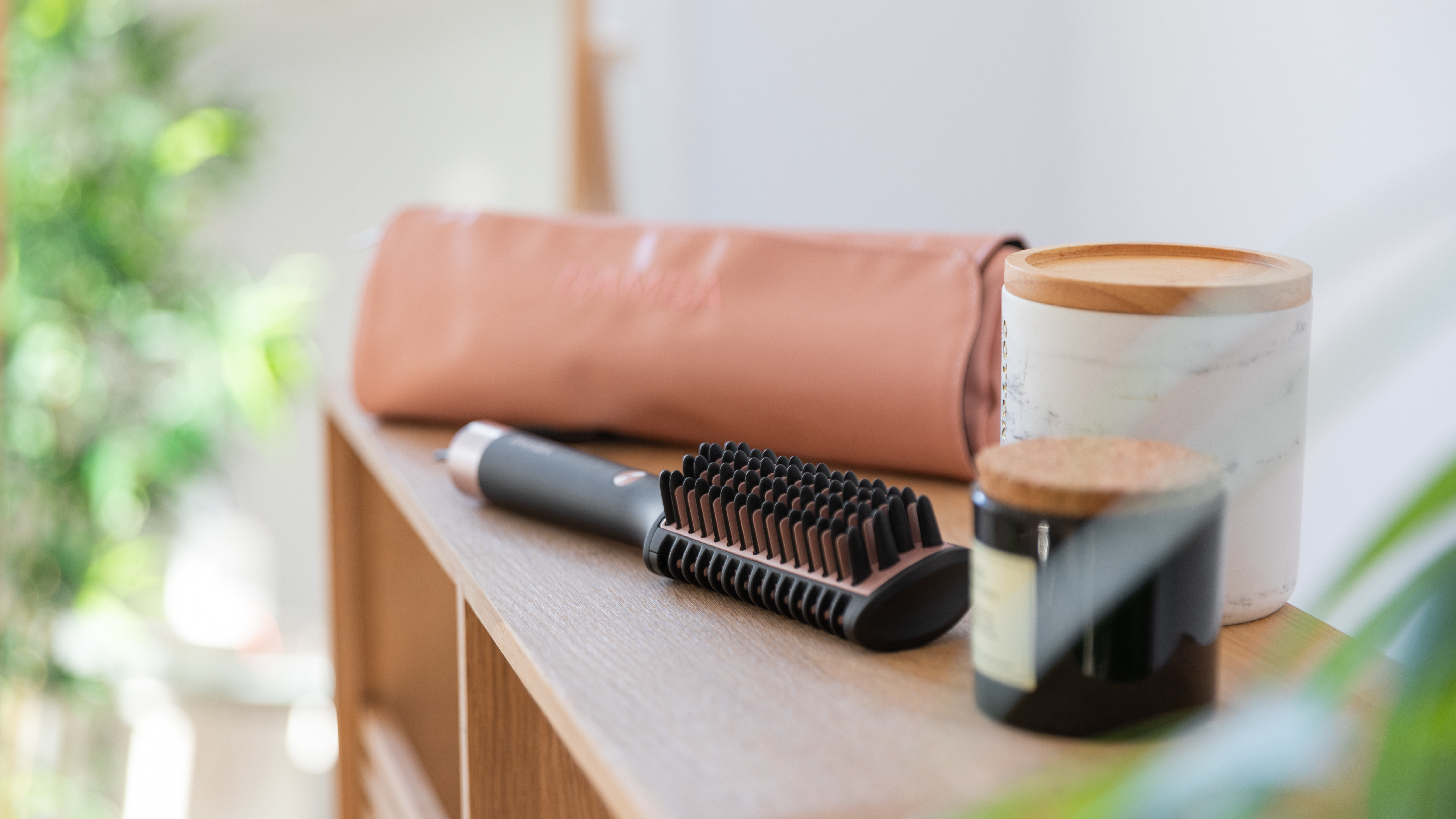 Herramientas de peinado: un cepillo para el cabello, una funda para rizador y dos velas decorativas en un estante.