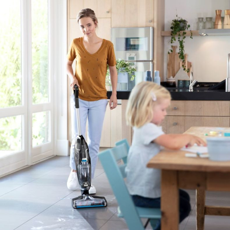 Vrouw die een Bissell-stofzuiger gebruikt, kind aan tafel.