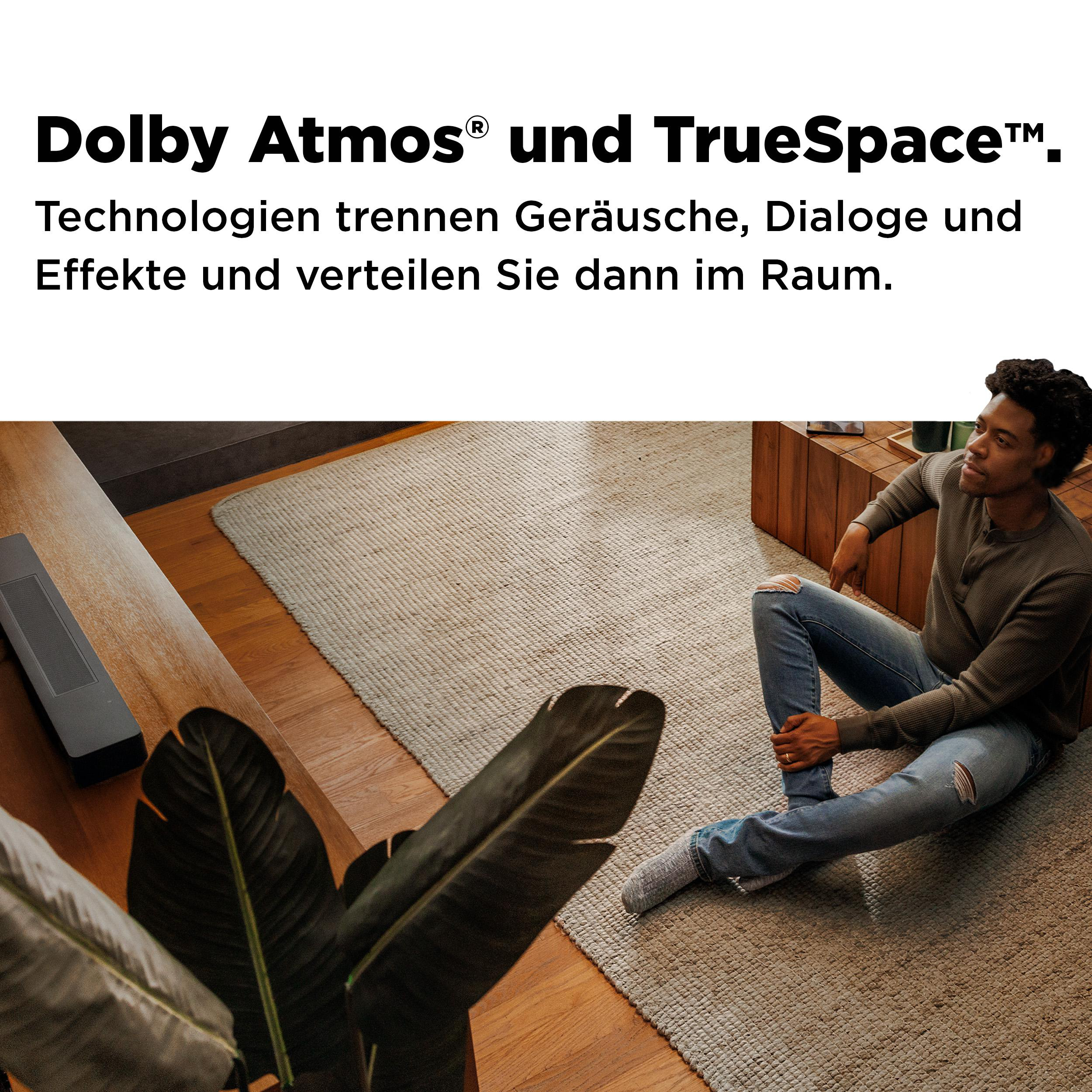 Ein Mann sitzt auf einem Teppich neben einem Holztisch mit Text über Dolby Atmos.