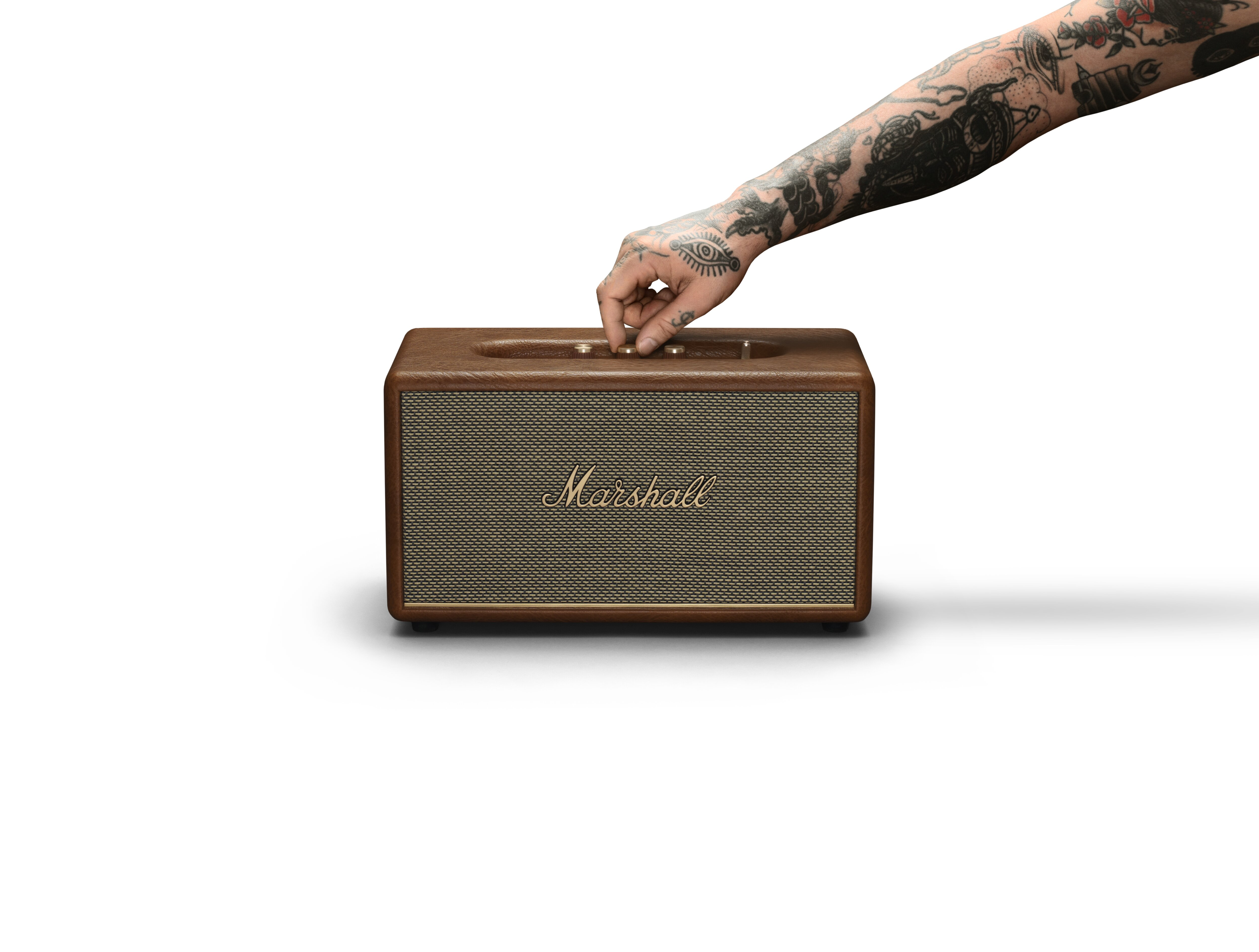 Tätowierter Arm bedient einen Marshall-Lautsprecher mit braunem Holzfinish.