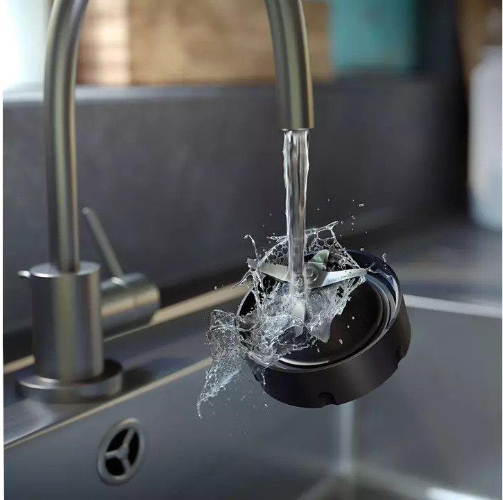 De l'eau éclaboussant une lame de blender dans un récipient noir dans un évier.