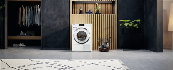 Secadora Miele blanca en interior moderno, con ropa y alfombra.