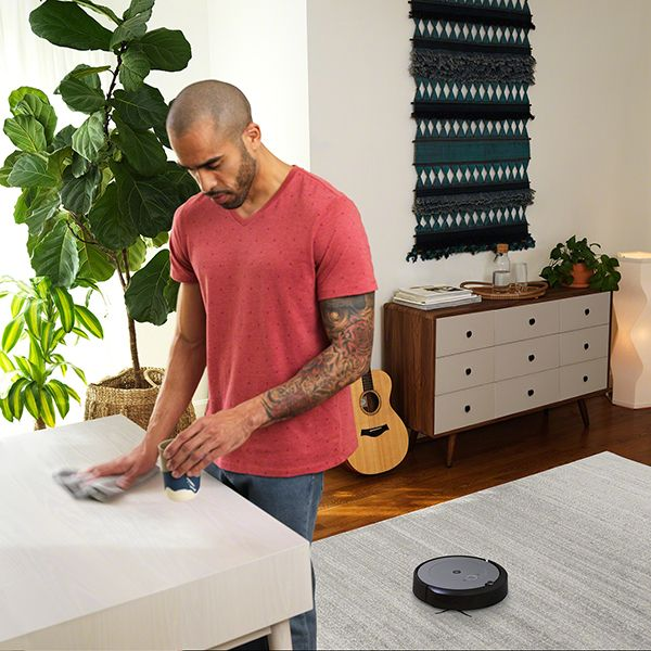Un homme nettoie une table avec un chiffon tandis qu'un aspirateur robot nettoie le sol. Intérieur de la maison.
