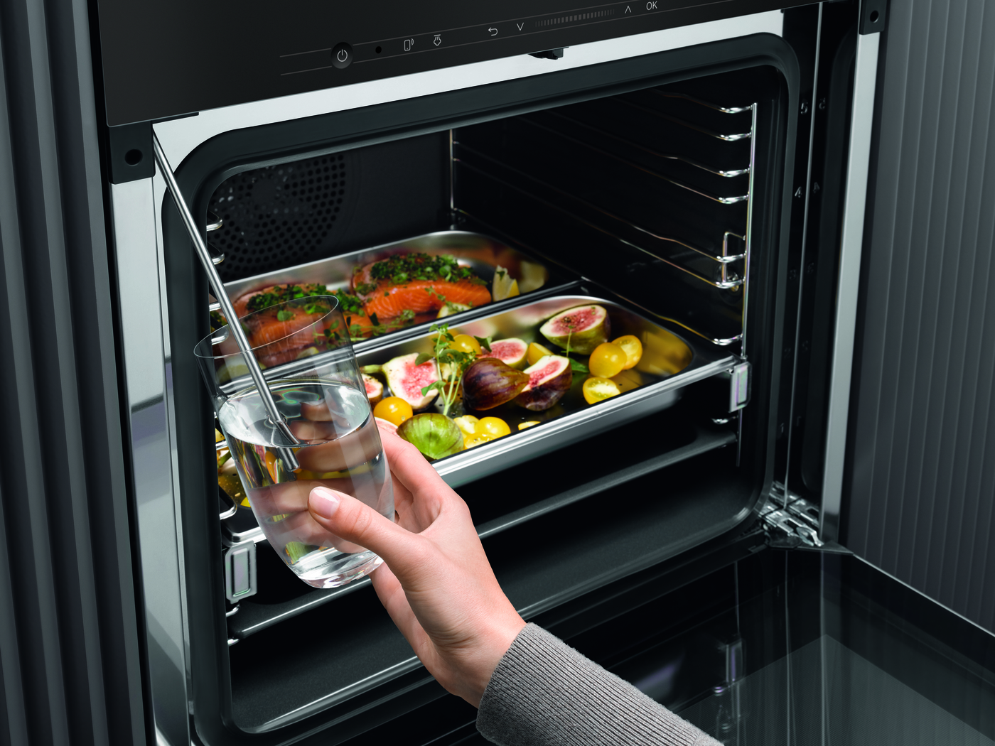 Oven met voedselbakken erin. Een persoon die een glas water vasthoudt. Donkere achtergrond.