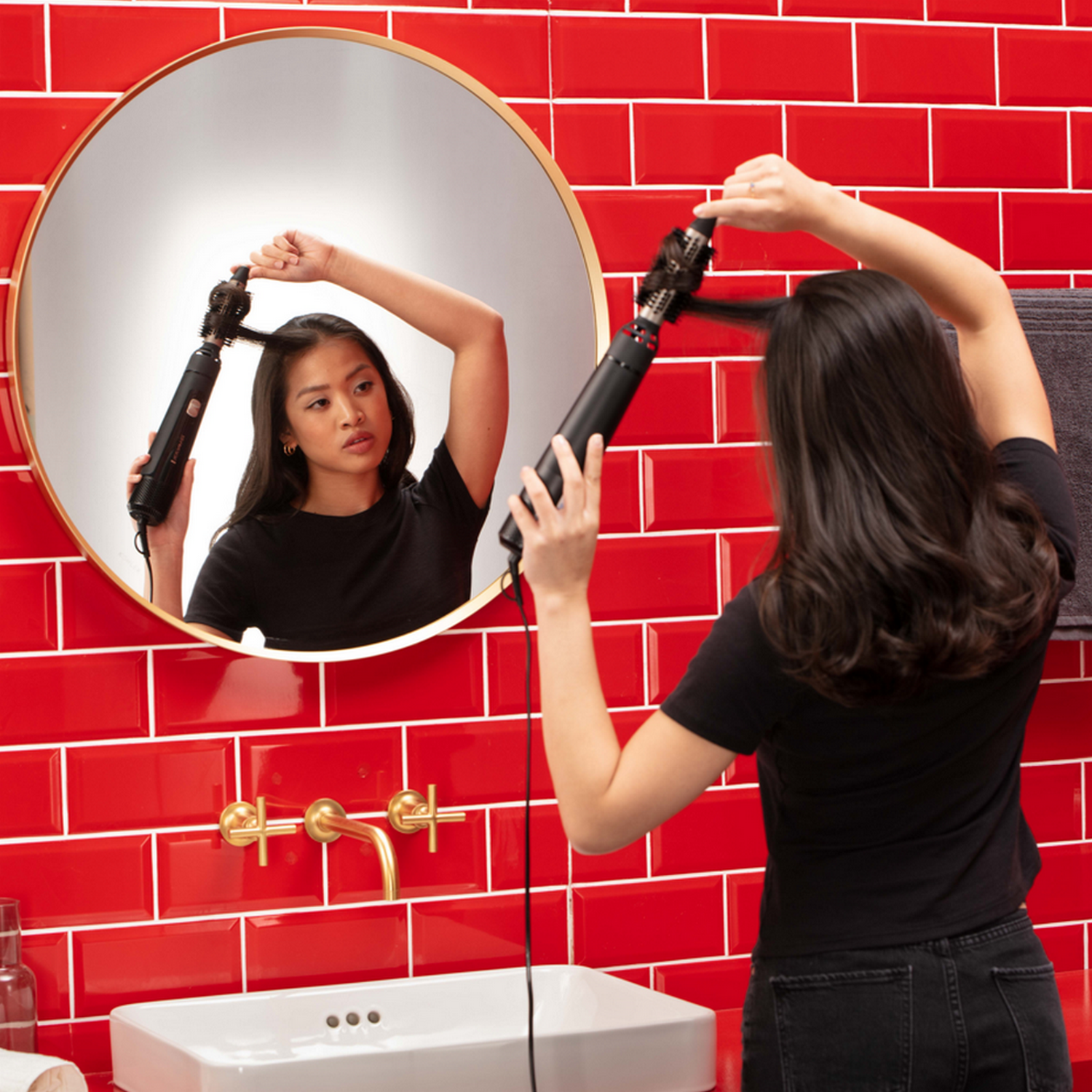Vrouw die haar krult voor een spiegel. Rode tegelwand.