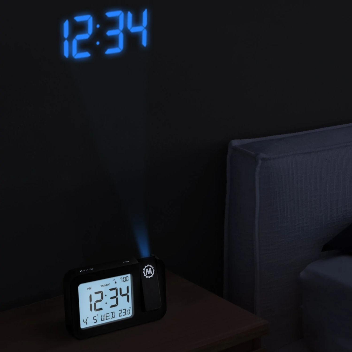 Black digital clock projecting time onto the wall; bedside table and bed are in the scene.