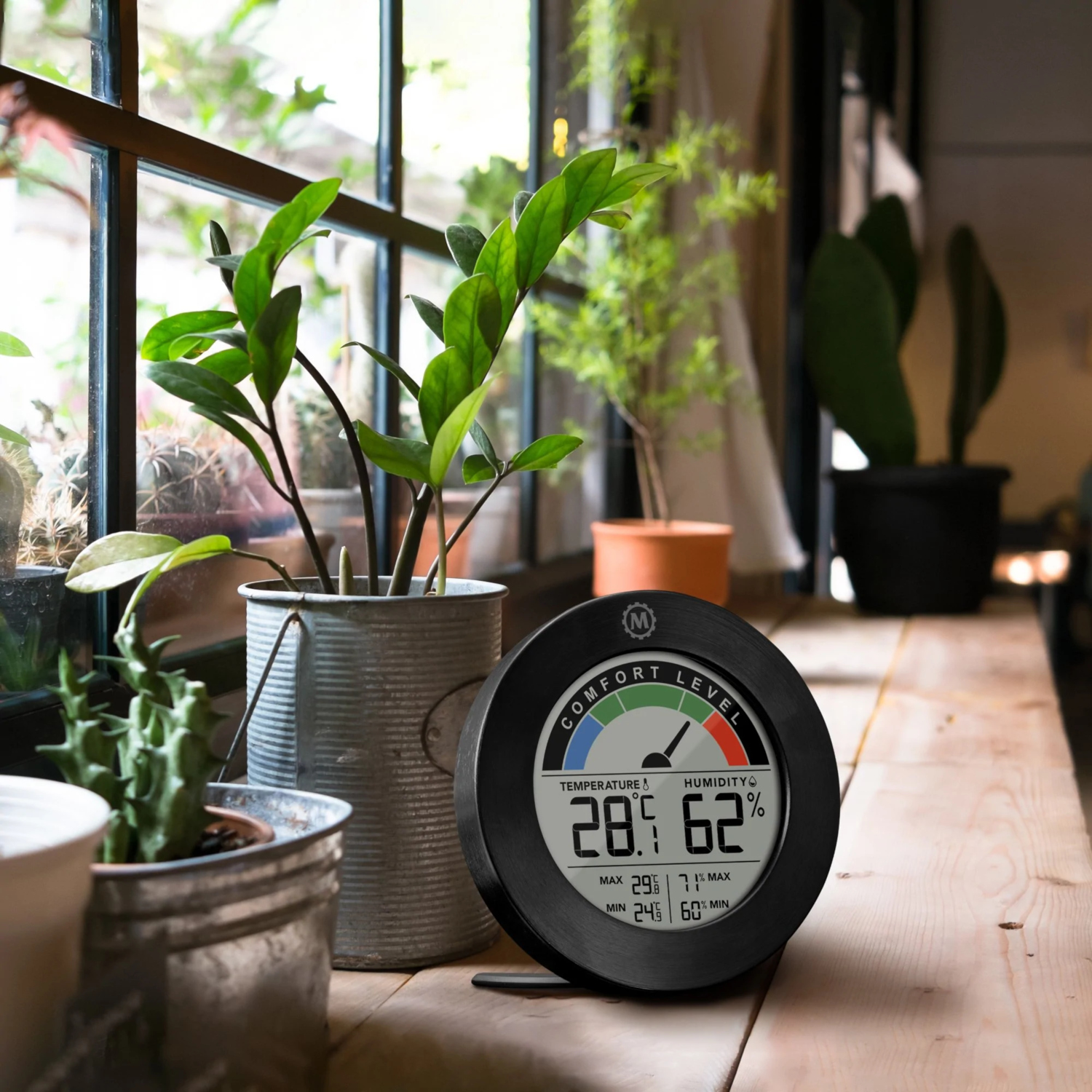 Thermometer on wooden table by plants near a window. Shows temperature and humidity levels.