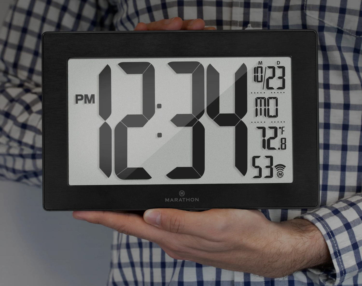 Une personne tenant une horloge numérique noire. L'horloge affiche l'heure, la date, la température et un signal Wi-Fi.