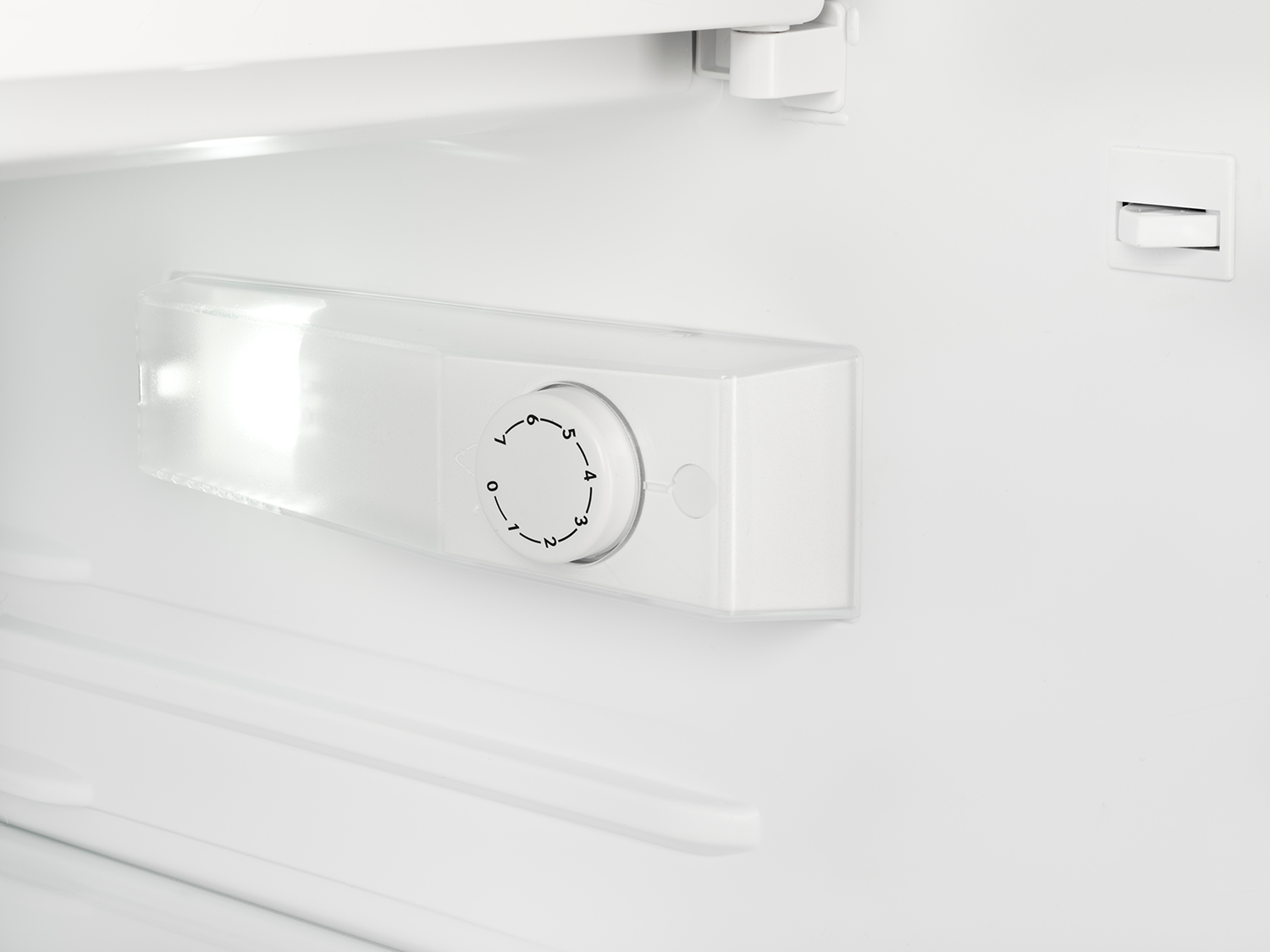 Inside of a white refrigerator. A white temperature control box with a dial from 1-7 is inside.